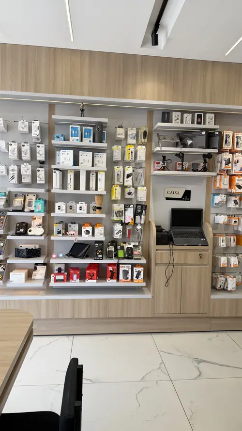 Parede de acessórios da IC Store com carregadores, cabos, fones e caixa de atendimento