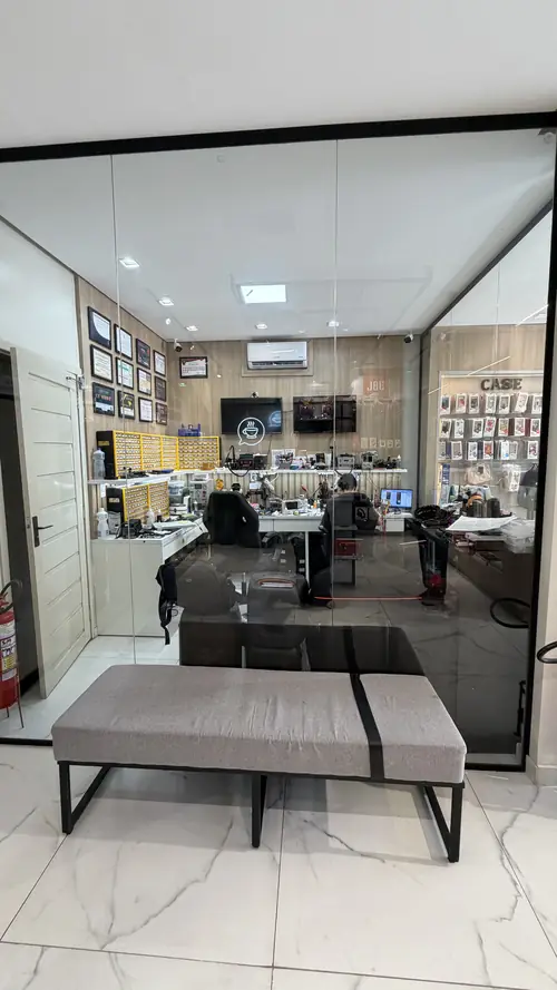 Bancada da IC Store vista de dentro da loja, separada por uma parede de vidro, com a parede de certificados ao fundo